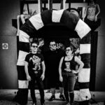 black and white image with Tommy on the left, Wyatt in the middle and Mimi on the right. They are under an arch made to look like the body of a sandworm from Beetlejuice.