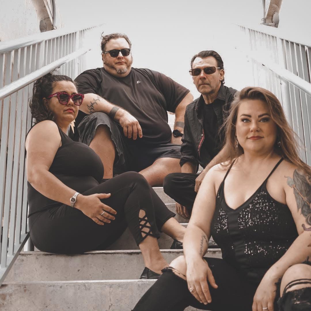 four members of the Bee Stings are all dressed in black sitting on stairs